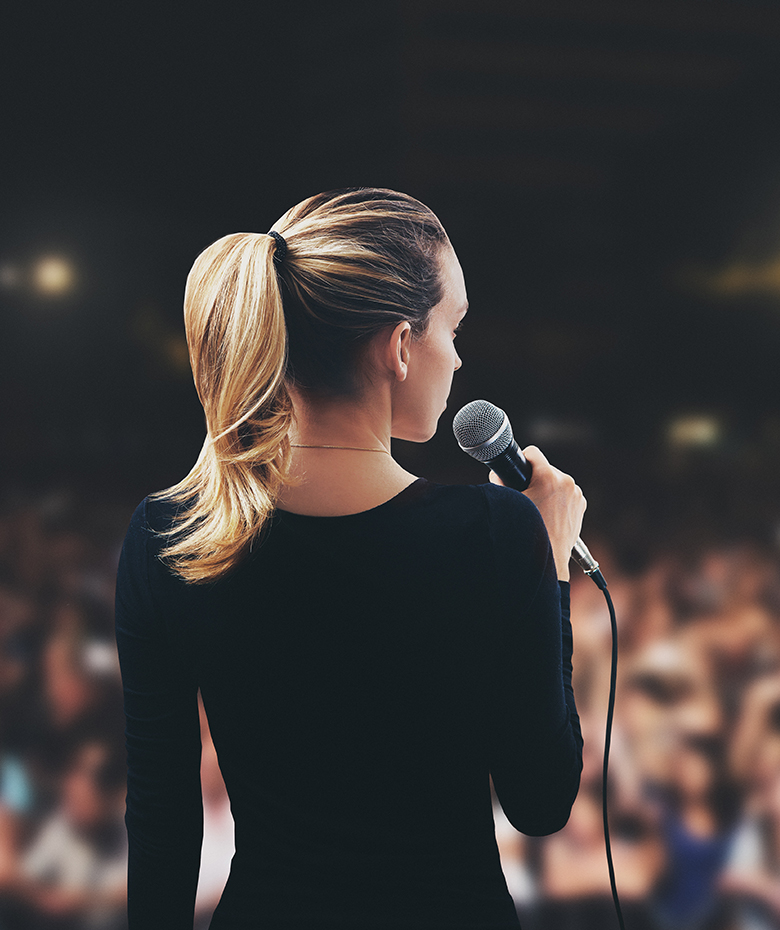 East meets West - Oprawa wizualna konferencji na żywo - prezenter z mikrofonem ; zdjęcie od tyłu; kobieta