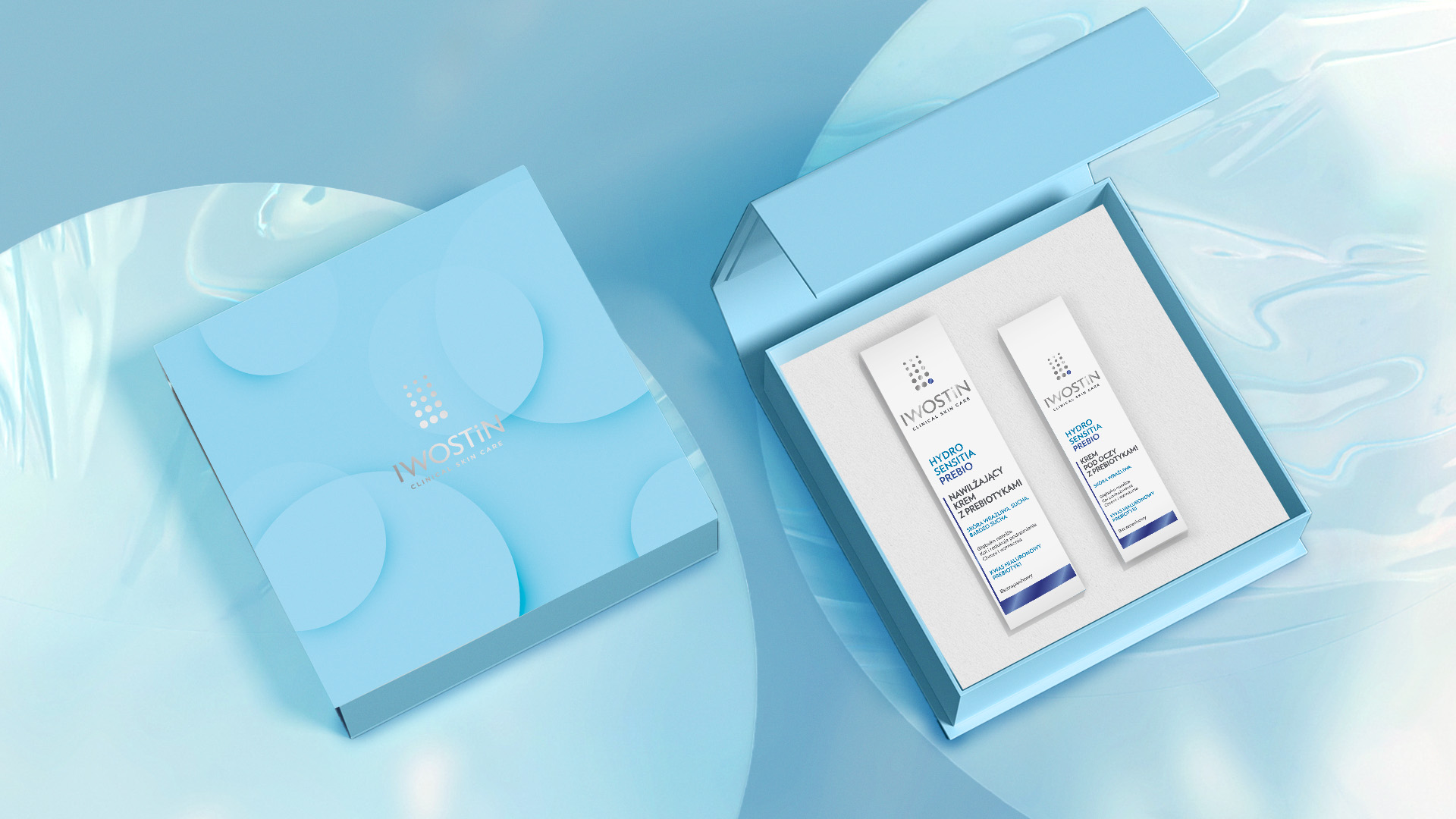 Iwostin opakowanie prezentowe - rzut od góry ; od lewej zamknięte opakowanie Iwostin, widoczne przenikające się okręgi z logo, całość niebieska; obok otwarte pudełko z pokazanym środkiem  - insert to dwa opakowania kosmetyków tworzących zestaw prezentowy