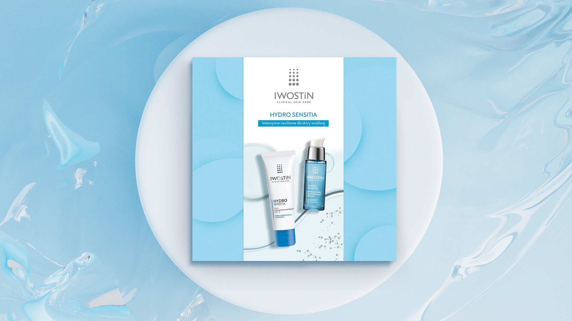 Iwostin opakowanie prezentowe - rzut od gory; opakowanie w centralnej części na białym kole wpisanym w niebieskie marmurowe tło; opakowanie kwadratowe, niebieskie z nałożoną owijką w pionie prezentującą dwa kosmetyki i logo